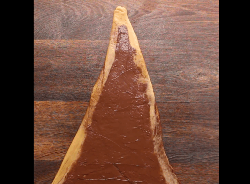 The third layer of chocolate spread onto the rectangle with the corners folded in, then rolled.